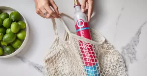 Kobieta wkłada do siatki zakupowej różowy cylinder CO2 typu Quick Connect SodaStream.